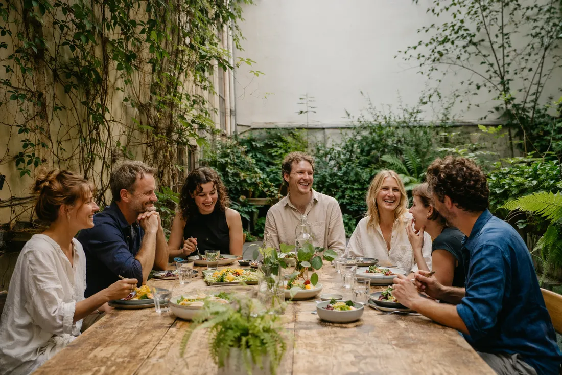 Friends sharing a relaxed daytime meal around a long communal table in a leafy Warsaw courtyard garden