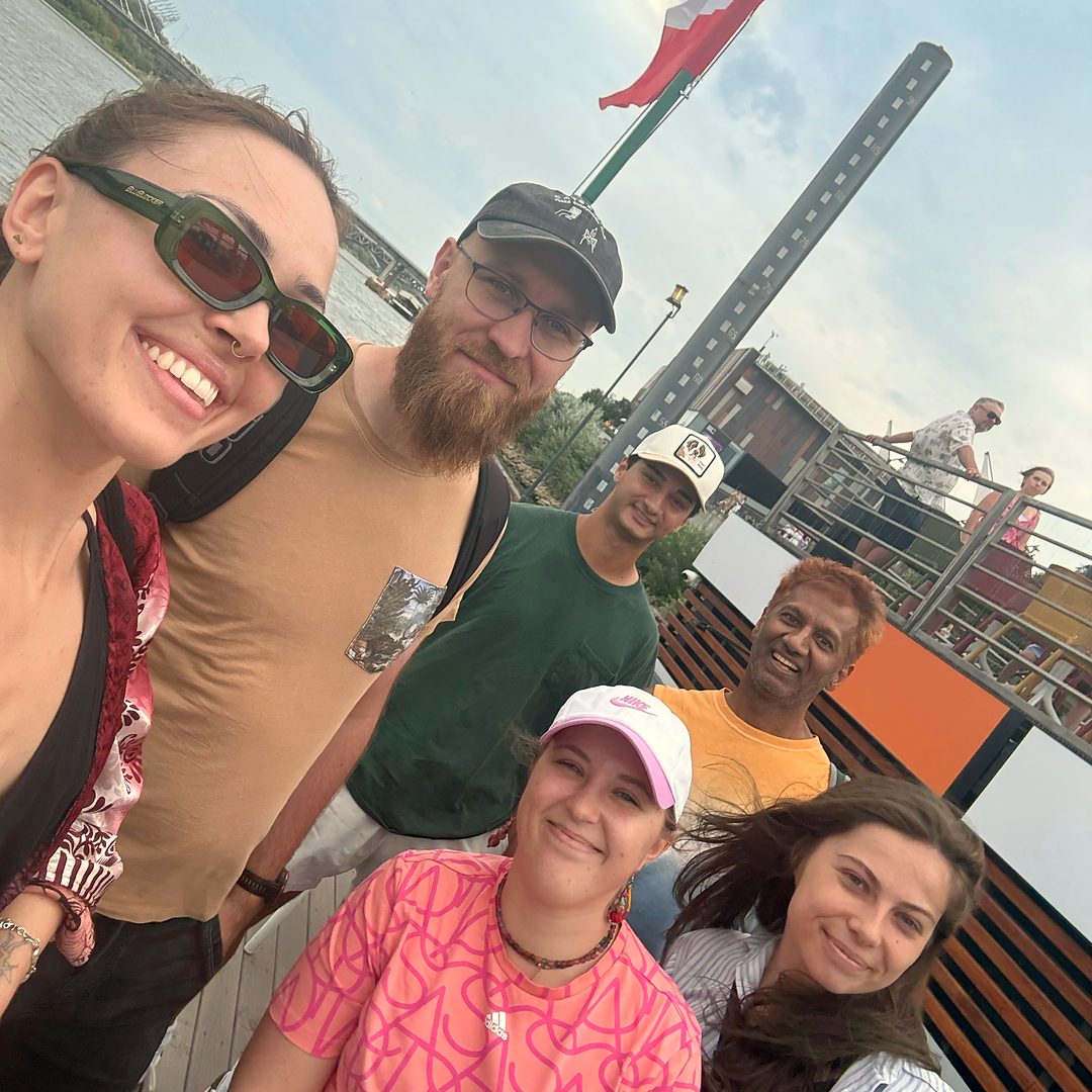 The Spotka team by the Vistula in Warsaw: six smiling people, with a bridge and a Polish flag behind them.